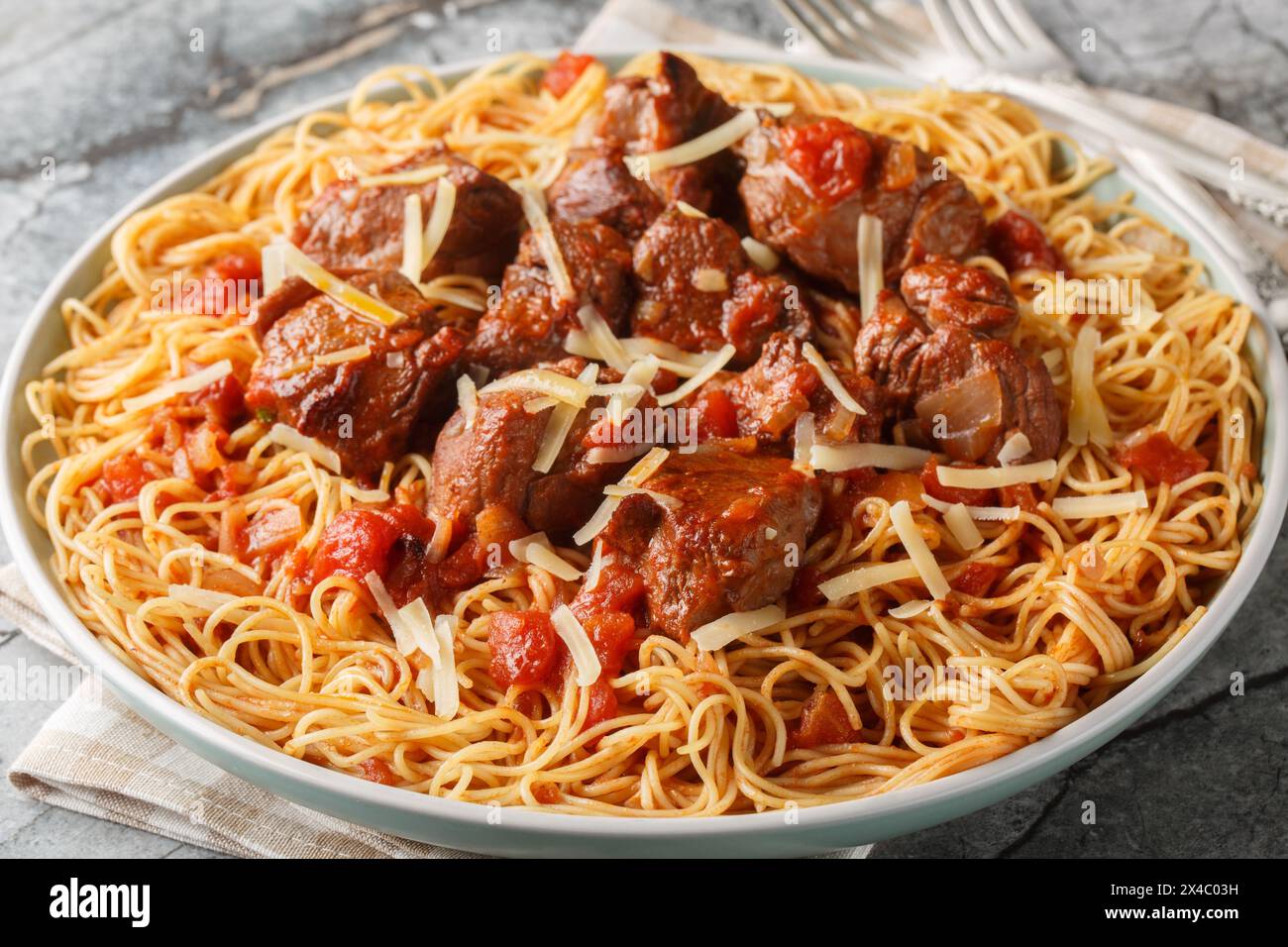 Moshari Kokkinisto o stufato di vitello greco Tas Kebap in salsa di pomodoro con primo piano di spaghetti di pasta sul piatto sul tavolo. Orizzontale Foto Stock