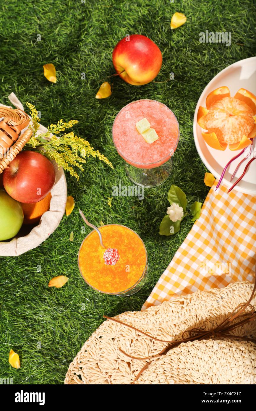 Scena pubblicitaria con concetto di vacanza al picnic. Vista dall'alto del cestino di frutta biologica decorato con due frullati freschi su uno sfondo di erba verde. CRE Foto Stock