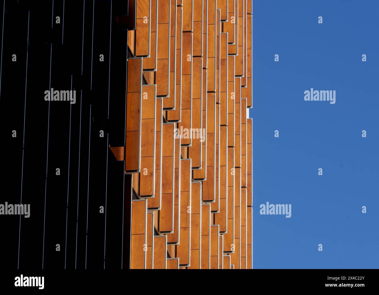 Mosaico di forme, motivi e colori sulla facciata di un edificio con finestre di legno arancione, con un cielo azzurro senza nuvole e metà dell'edificio Foto Stock