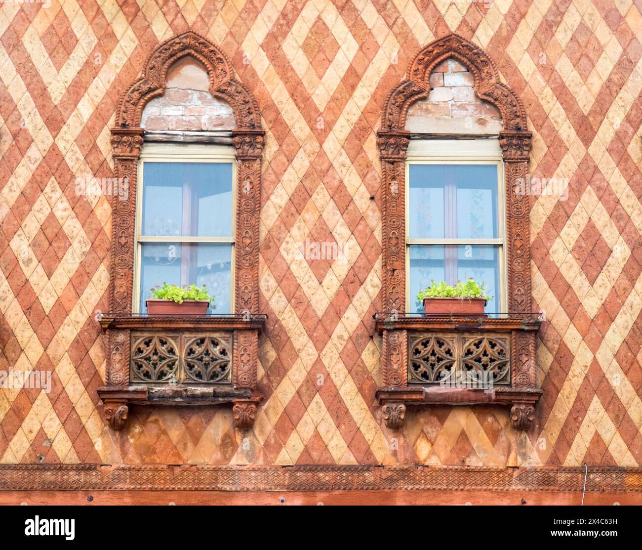 Italia, Venezia. Tipiche finestre veneziane con fiori su un muro di piastrelle molto colorato. Foto Stock