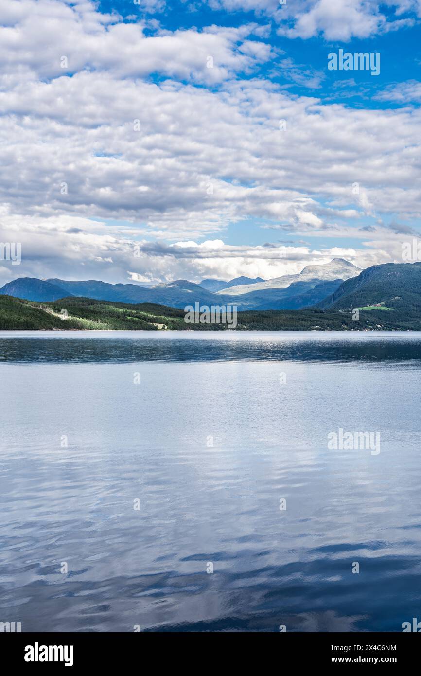 Affacciato sulle acque calme del Ålvundfjord. Vista sulla costa dei fiordi con un villaggio sullo sfondo delle montagne del Trollheimen in Norvegia Foto Stock