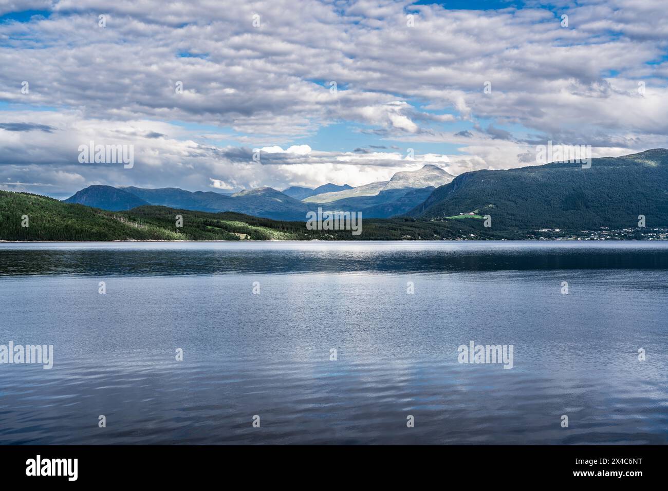 Affacciato sulle acque piatte e tranquille del Ålvundfjord. Vista sulla costa dei fiordi con un villaggio sullo sfondo dei monti Trollheimen in Norvegia Foto Stock