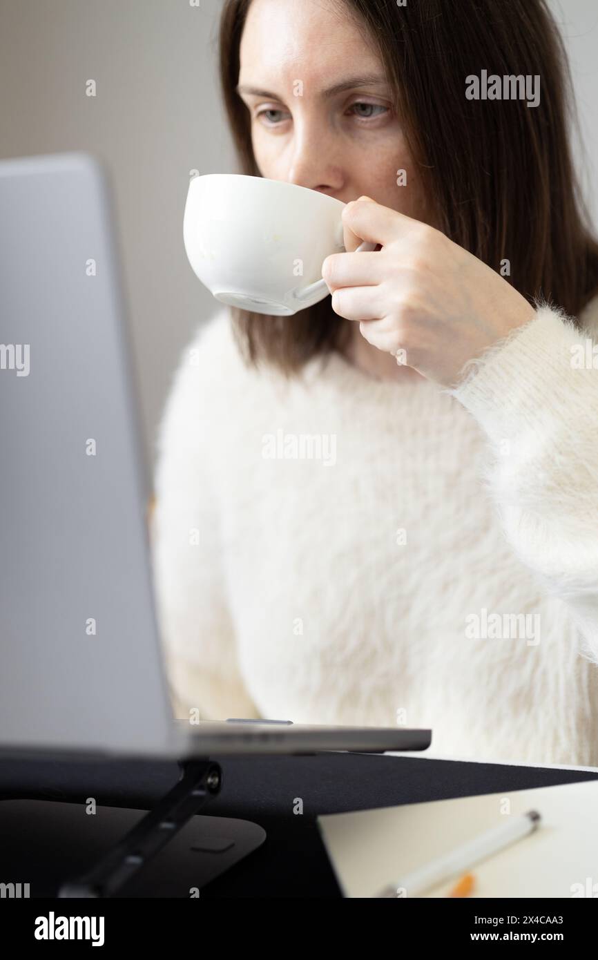 Donna che beve un caffè davanti allo schermo del notebook Foto Stock