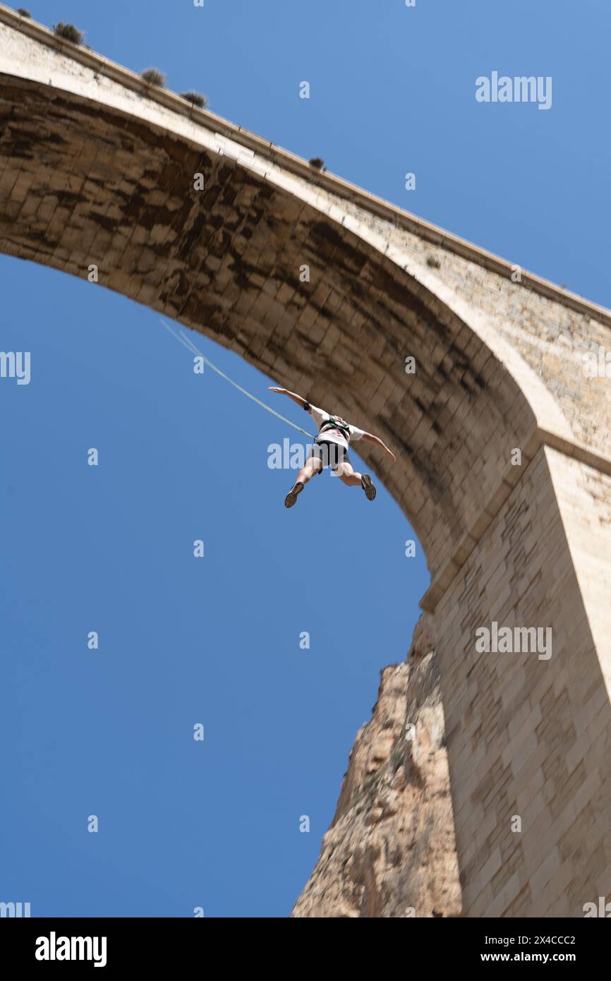Vista dall'angolo basso di una persona che salta da uno storico ponte di pietra. Concetto di sport d'avventura. Nessuna paura Foto Stock
