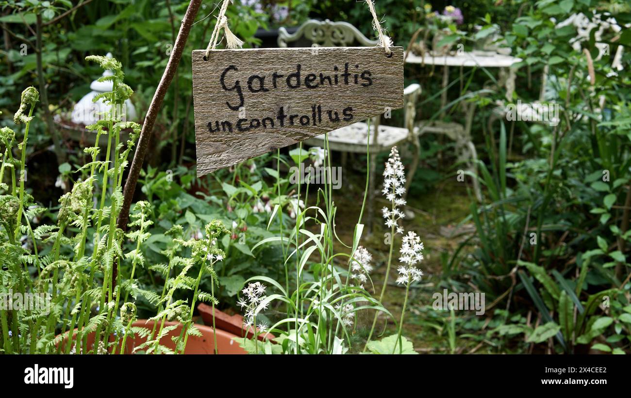 Una tavola di legno in un giardino che dice: "Giardinaggio incontrollabile”. Foto Stock