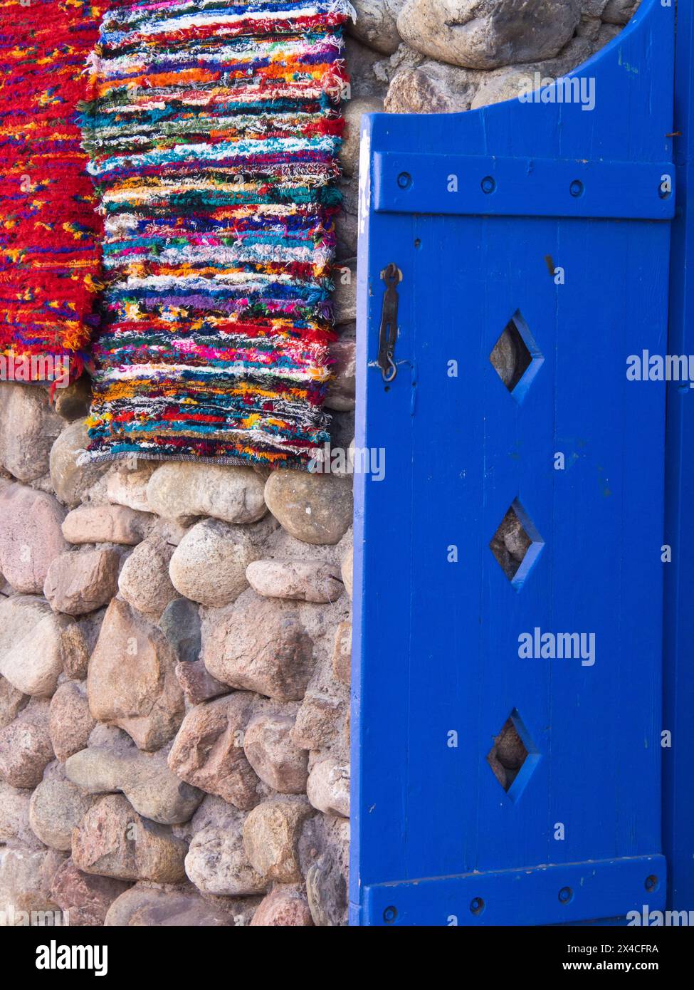 Stati Uniti, nuovo Messico, Sante Fe. Otturatore colorato blu brillante e tessuti fatti a mano appesi su un muro di pietra. Foto Stock