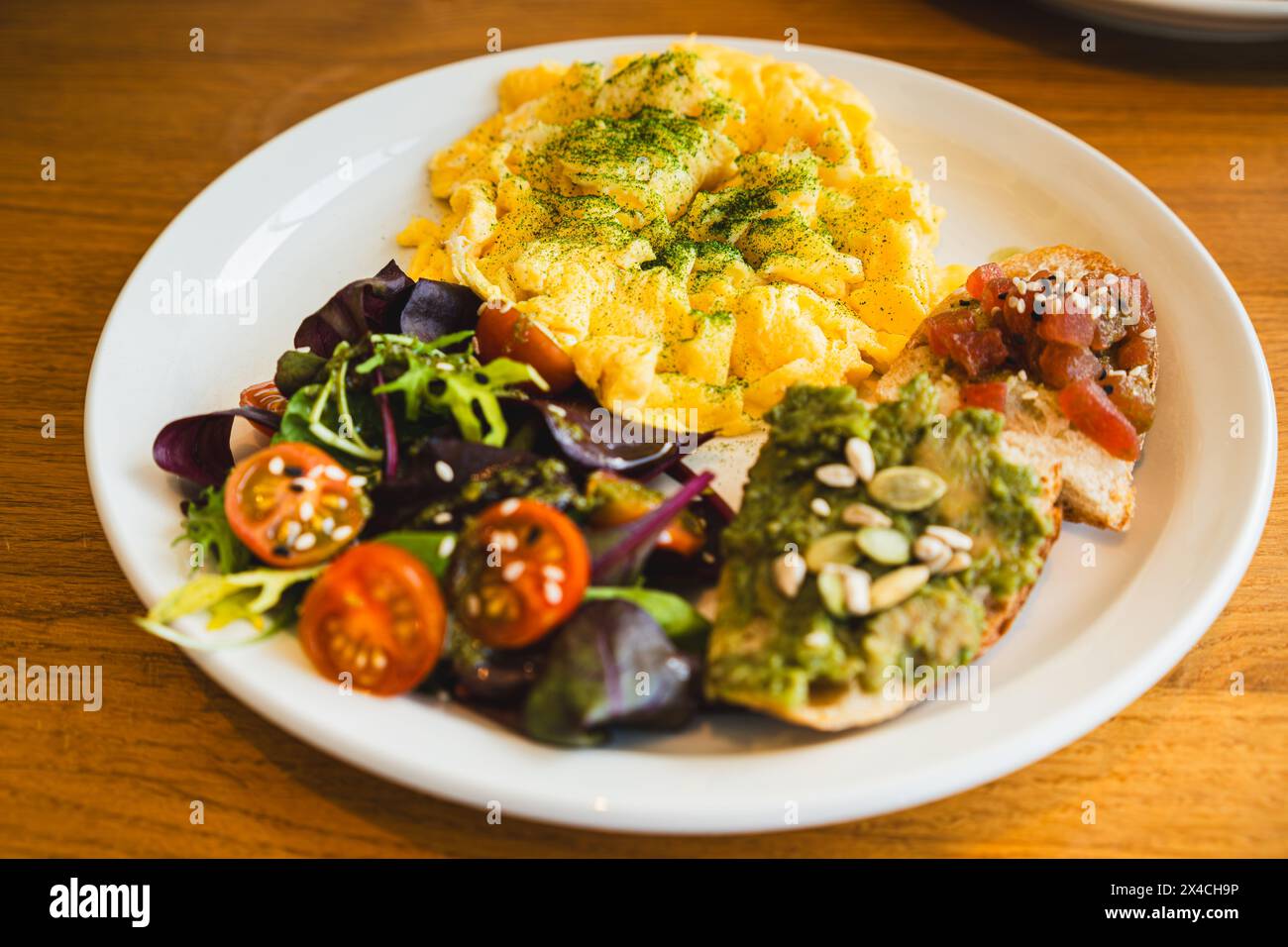 Un nutriente brunch servito con soffici uova strapazzate, una vibrante insalata mista, pane tostato all'avocado e semi Foto Stock