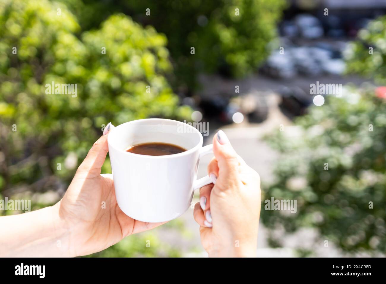 Una giovane donna si gode una tazza di caffè appena fatto sul balcone del suo appartamento. Foto Stock