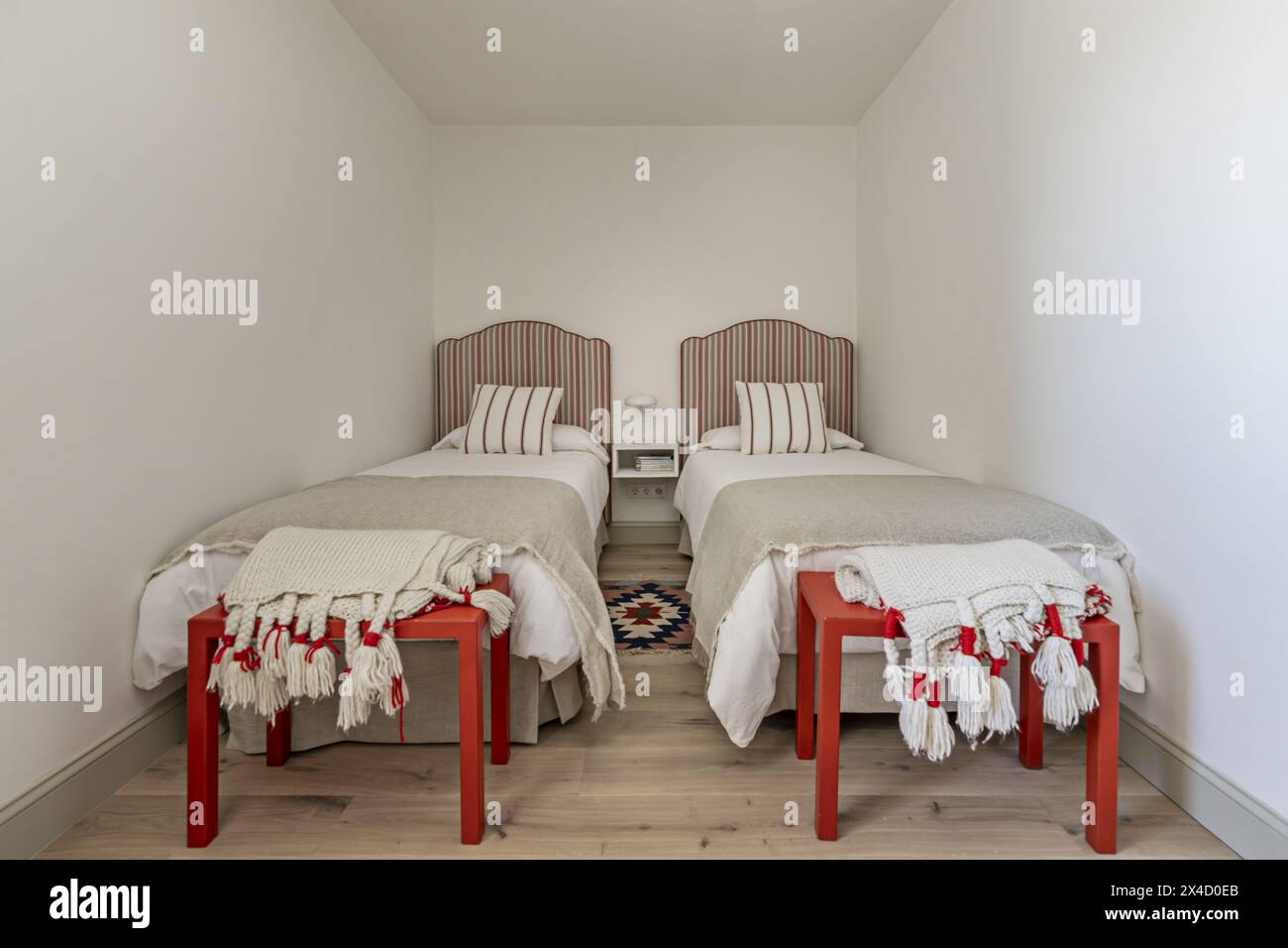 Una camera con due letti singoli con testiere rivestite in tessuto a righe rosse, cuscini e cuscini coordinati e un comodino centrale in legno Foto Stock