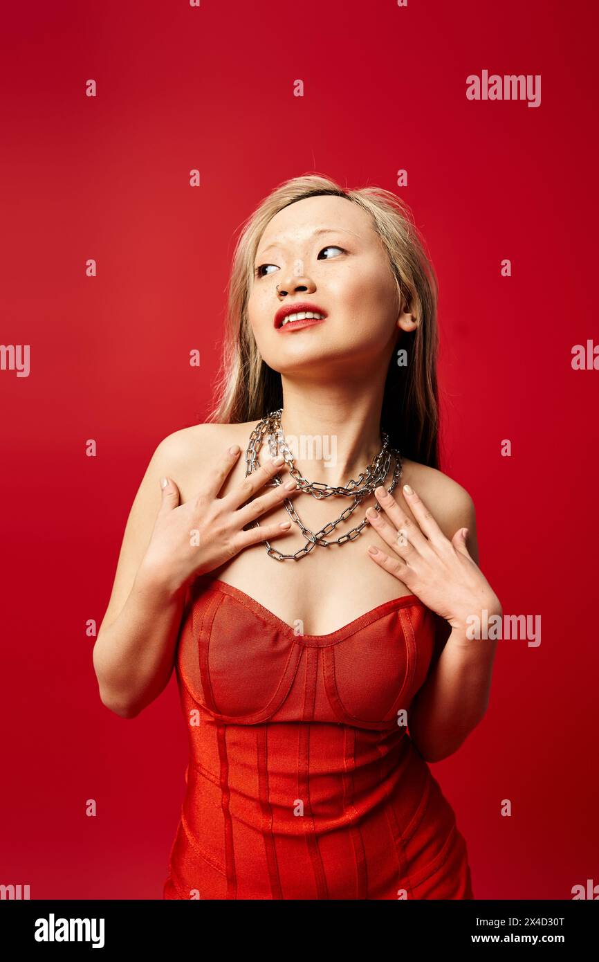 Una donna asiatica attraente posa con sicurezza in un vivace vestito rosso. Foto Stock