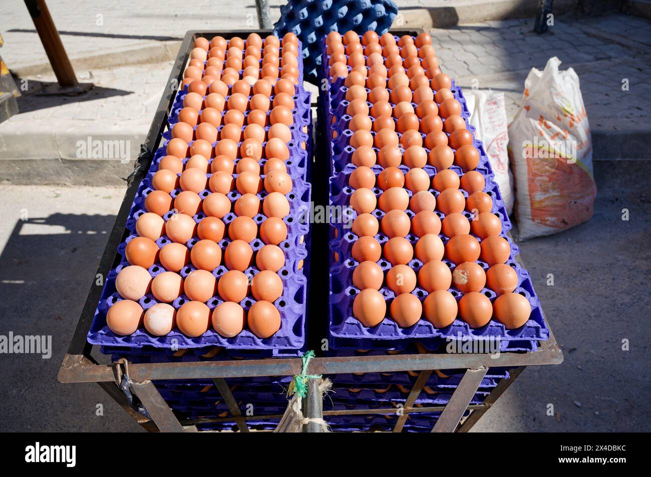 Dozzine di cartoni di uova impilati in alto su una strada di FES, gli strati superiori bagnati dalla luce del sole, rendendo brillanti le gusci d'uovo. Foto Stock