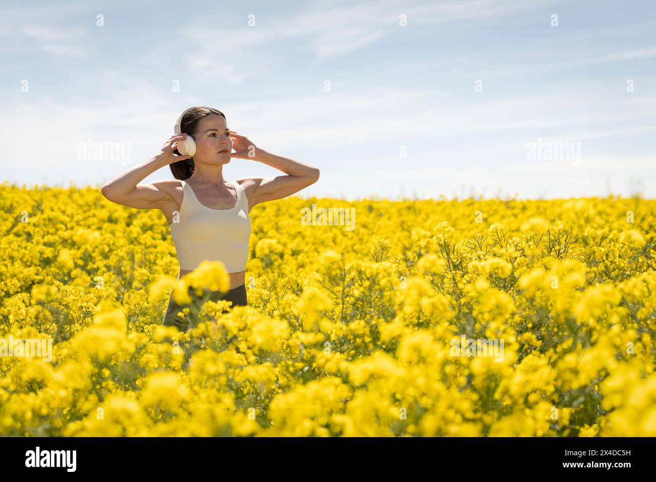 Donna rilassata che ascolta la musica con le cuffie in un campo giallo, primavera estate. Foto Stock