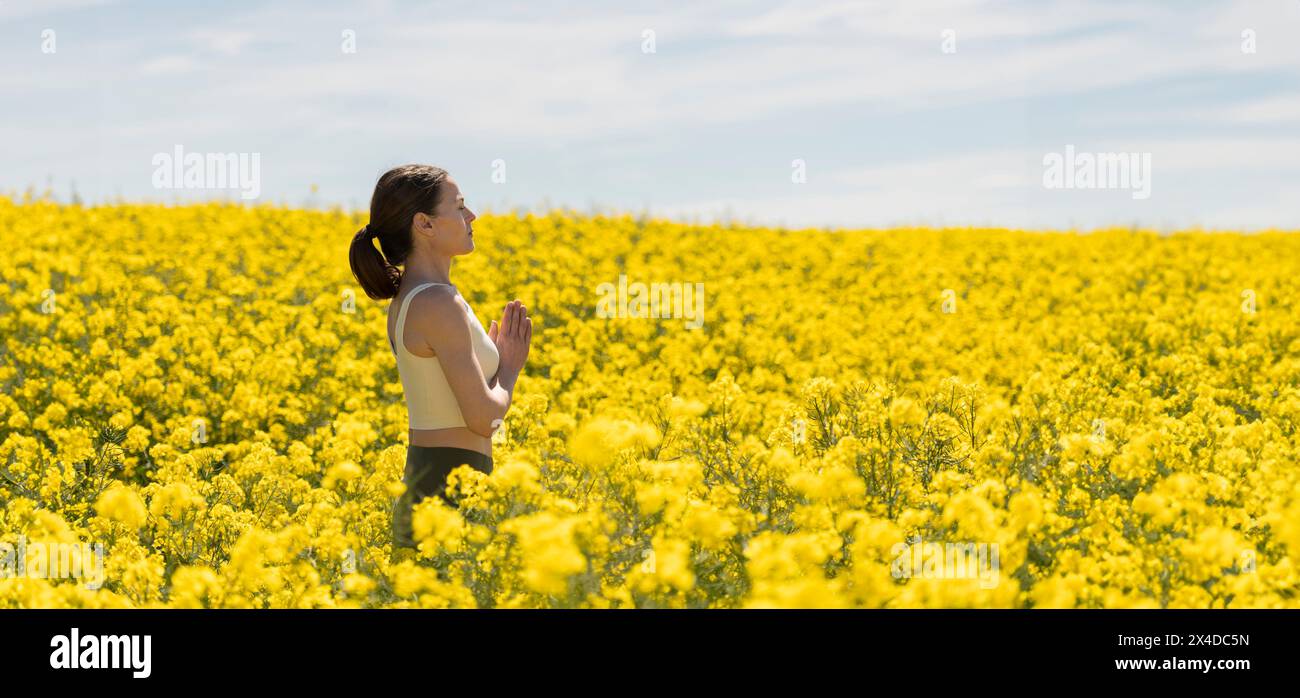 Donna che respira aria fresca in un campo giallo e pratica la meditazione yoga Foto Stock