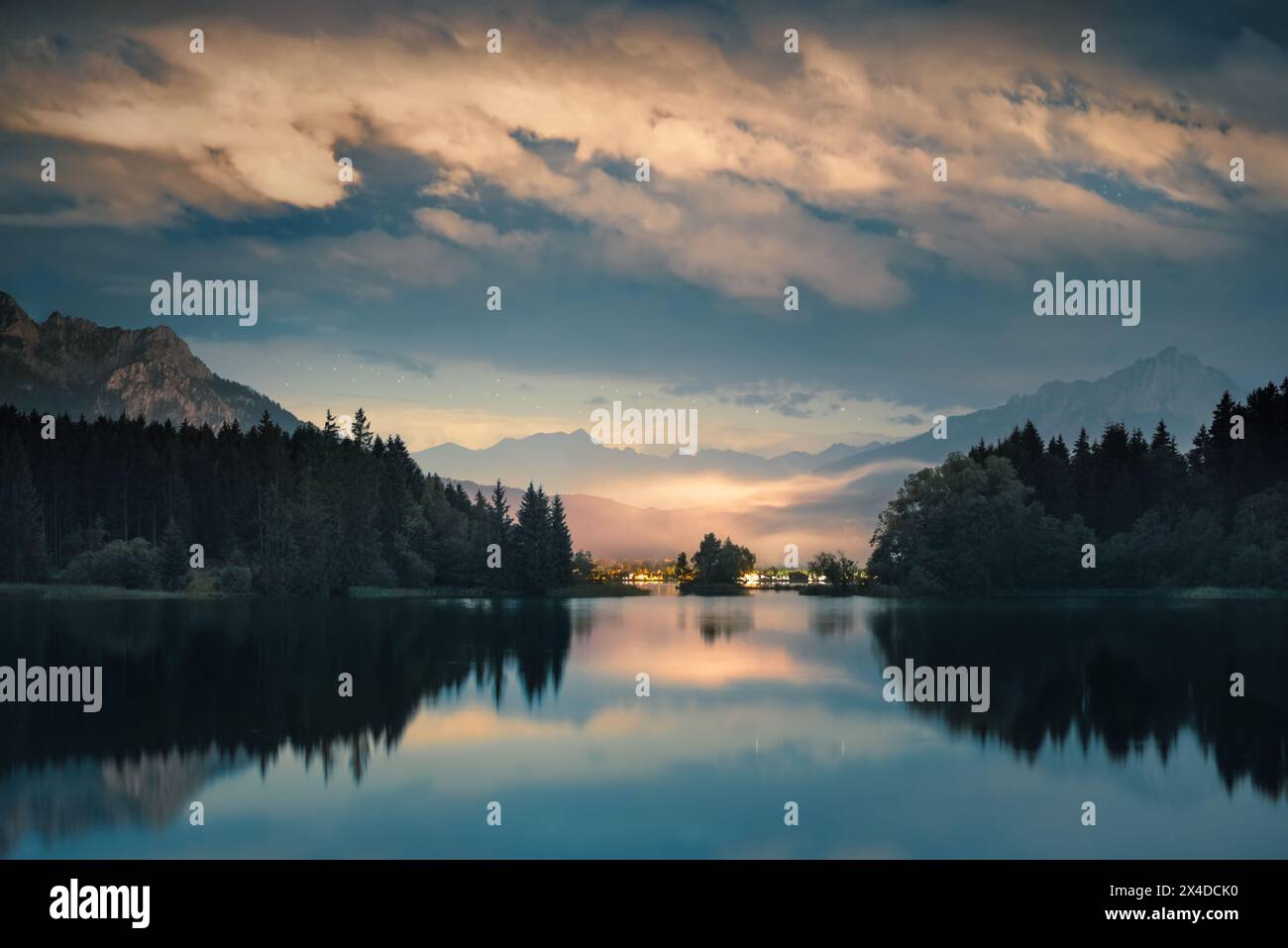 Scenario notturno con nuvole illuminate riflesse in un lago. Un tranquillo paesaggio alpino dai toni blu e gialli Foto Stock