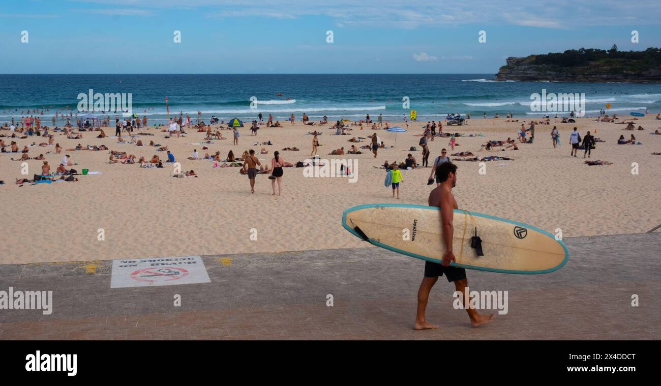 Un surfista porta la sua tavola da surf oltre Bondi Beach a Sydney, Australia Foto Stock