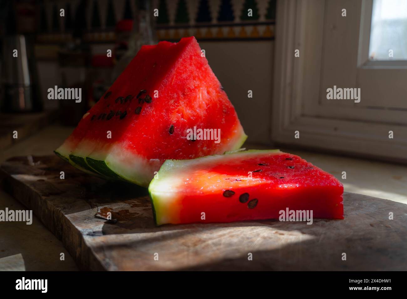 L'anguria fresca e colorata sul tavolo della cucina, parzialmente illuminata dalla luce del sole della finestra. Foto Stock