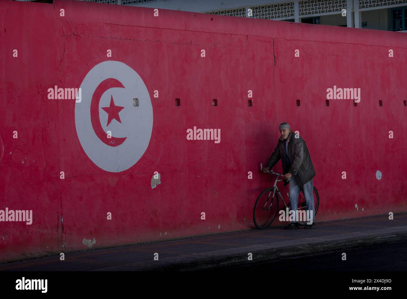 L'uomo con la bicicletta che passa accanto al muro con la bandiera tunisina nella città di Biserta. Foto Stock