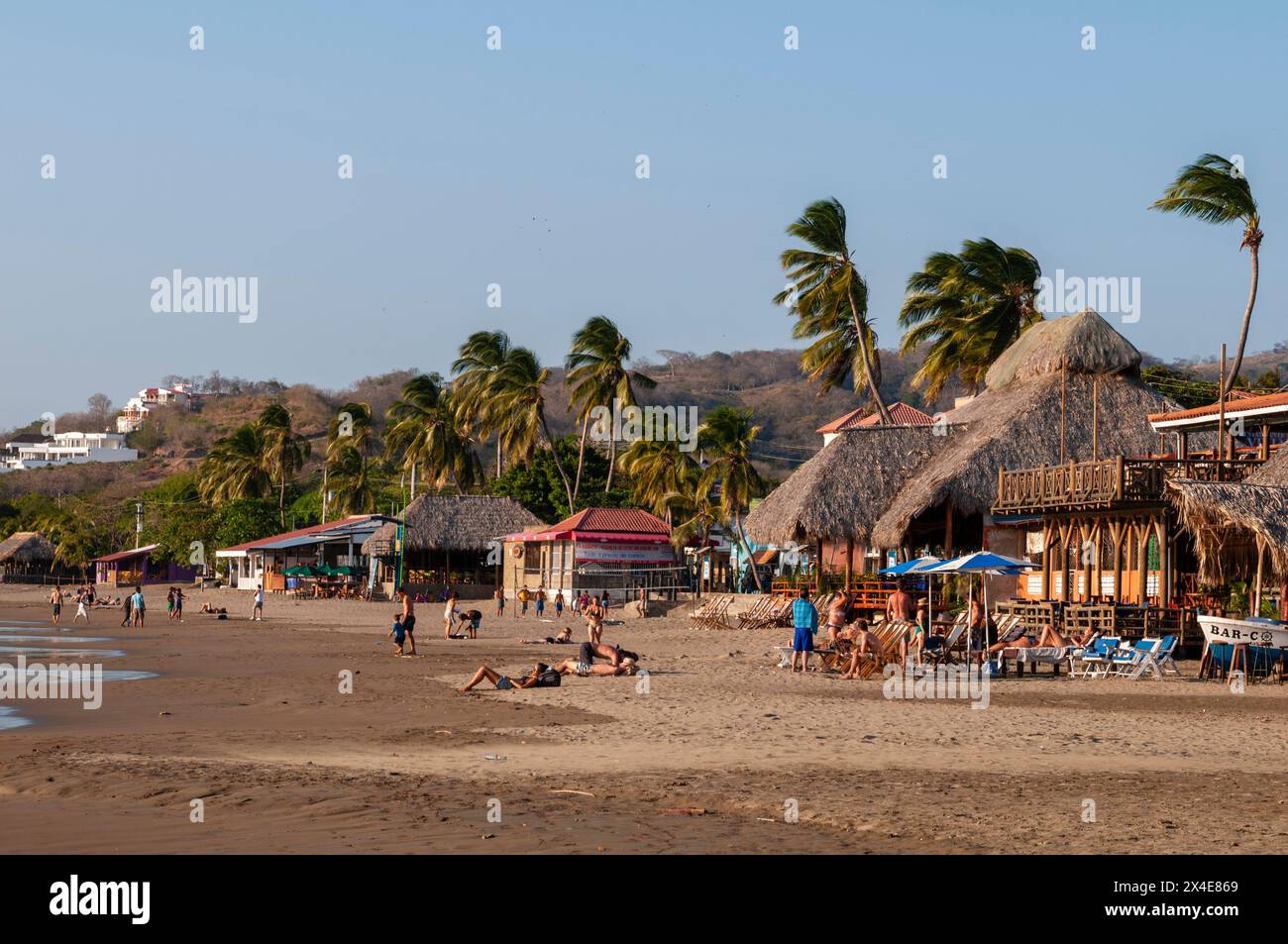 Palme soffiate dal vento, capanne con tetto di paglia e bagni di sole su una spiaggia sabbiosa. San Juan del Sur, Nicaragua. (Solo per uso editoriale) Foto Stock
