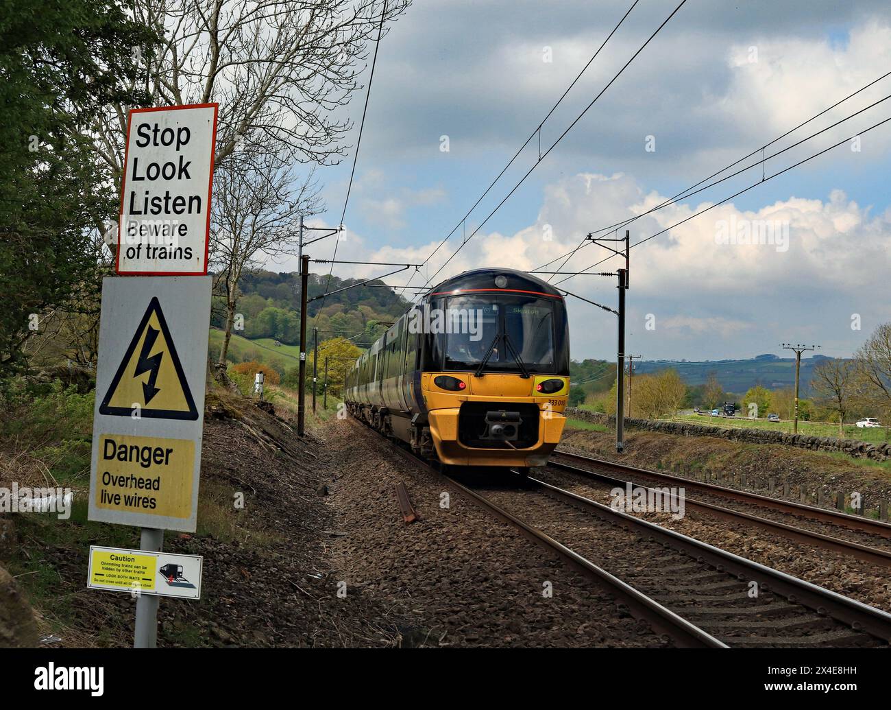 Un treno elettrico del Nord passa i segnali di sicurezza ad un passaggio a piedi sopra la ferrovia alla fine di Parkers Lane a Low Utley nella valle dell'Aire. Foto Stock