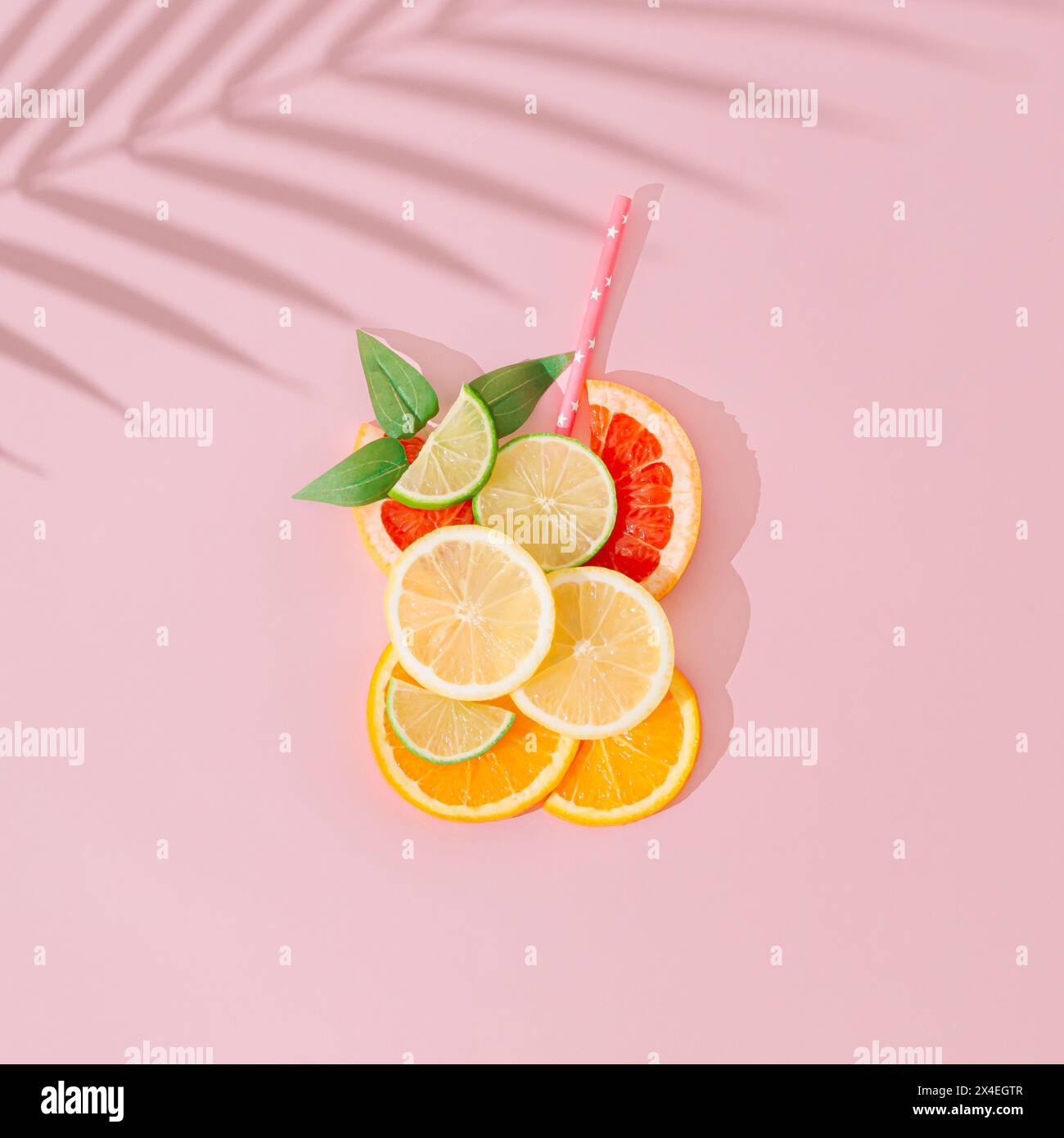 Bicchiere di bevanda rinfrescante a base di fette di limone, lime, arancia e pompelmo, paglia e foglie verdi con ombra di foglie di palma su sfondo rosa. Foto Stock