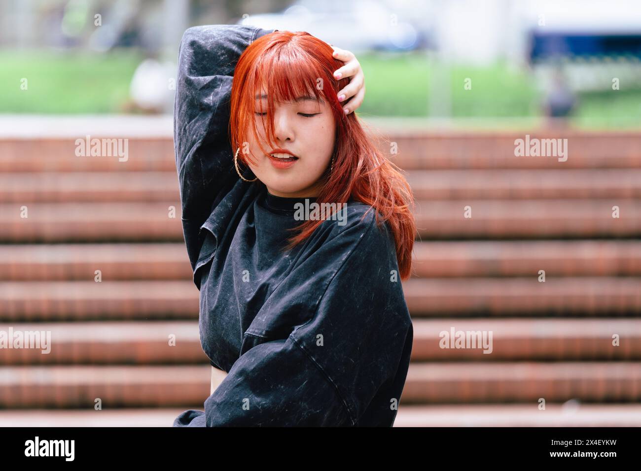 Ballerina coreana appassionata con i capelli rossi nel flusso della sua routine in un ambiente urbano all'aperto Foto Stock