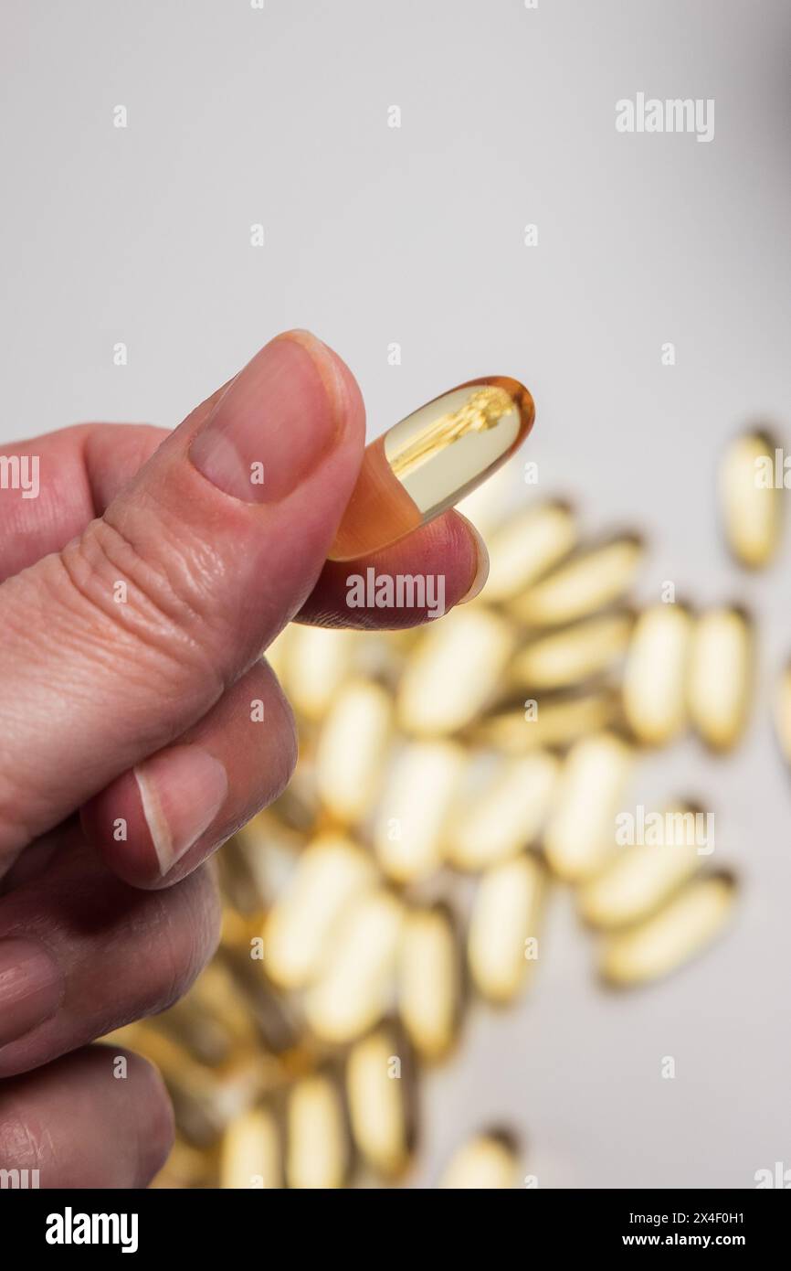 mano della donna che tiene in mano una pillola di olio di pesce con omega 3 di colore giallo dorato, un nutriente essenziale Foto Stock