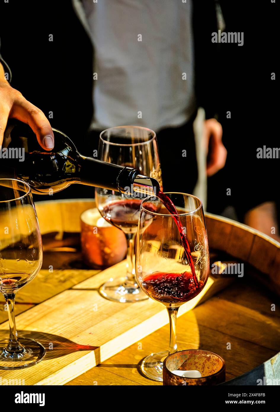 Stati Uniti, Stato di Washington, Bothell. L'uomo versa del vino rosso in un bicchiere alla luce del sole su una botte. Foto Stock