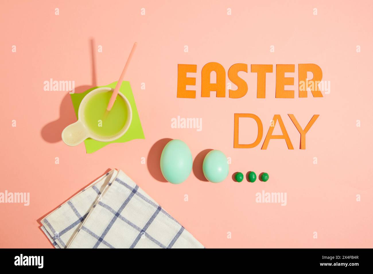 Su sfondo rosa, testo "giorno di Pasqua" decorato con uova blu e caramelle al cioccolato verde. Scena minimale con vista dall'alto per la pubblicità Foto Stock