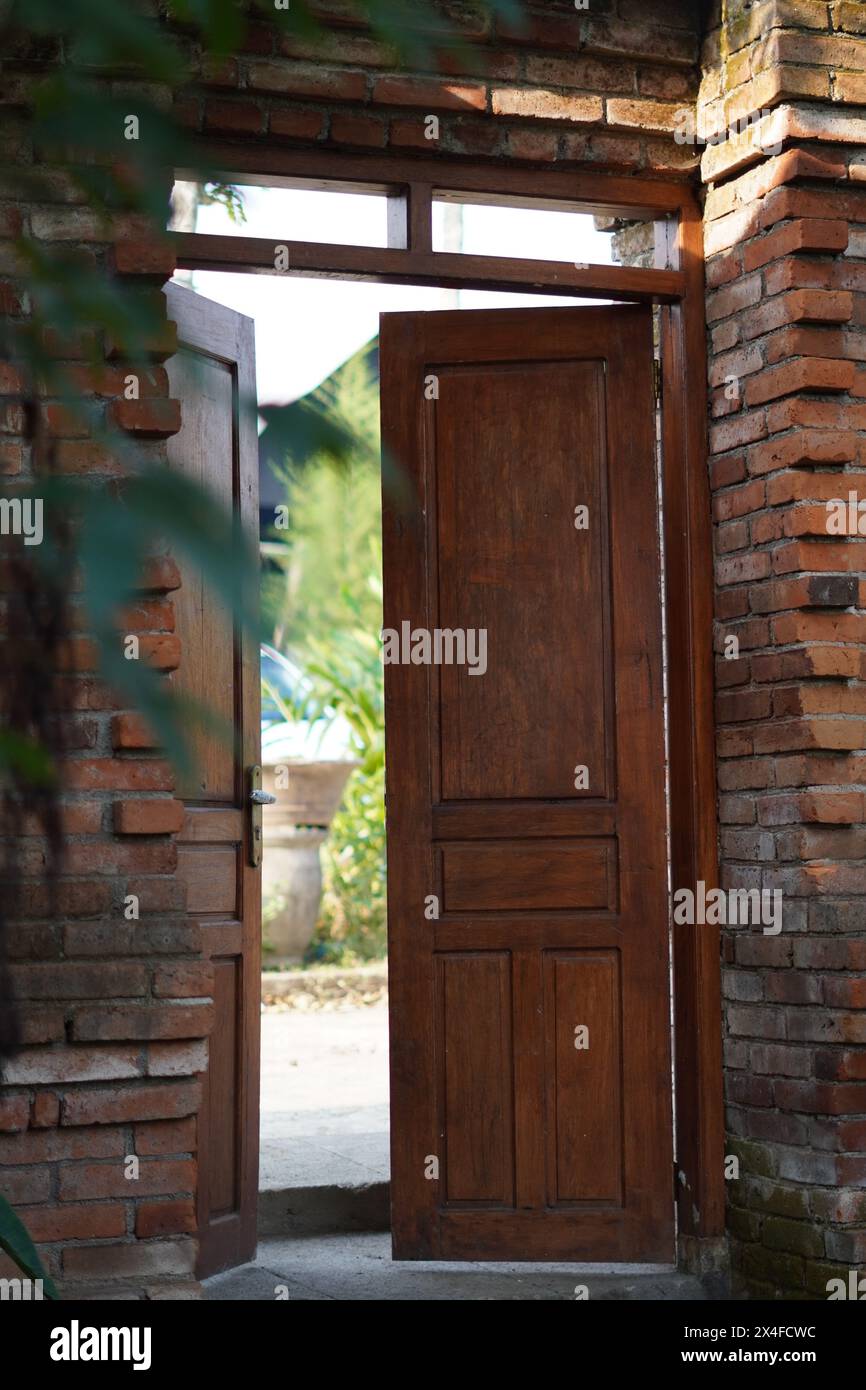Porta di legno tradizionale aperta con telaio in mattoni rossi con foglie verdi sfocate Foto Stock
