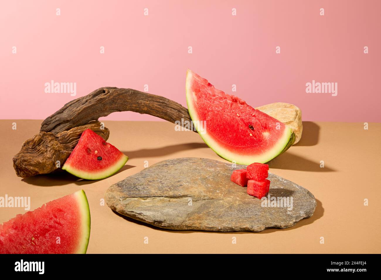 Su sfondo rosa, fresche fette di anguria decorate con ramoscelli essiccati e pietra grigia. Spazio per il prodotto da esposizione. Ricco di antiossidanti, l'anguria è Foto Stock