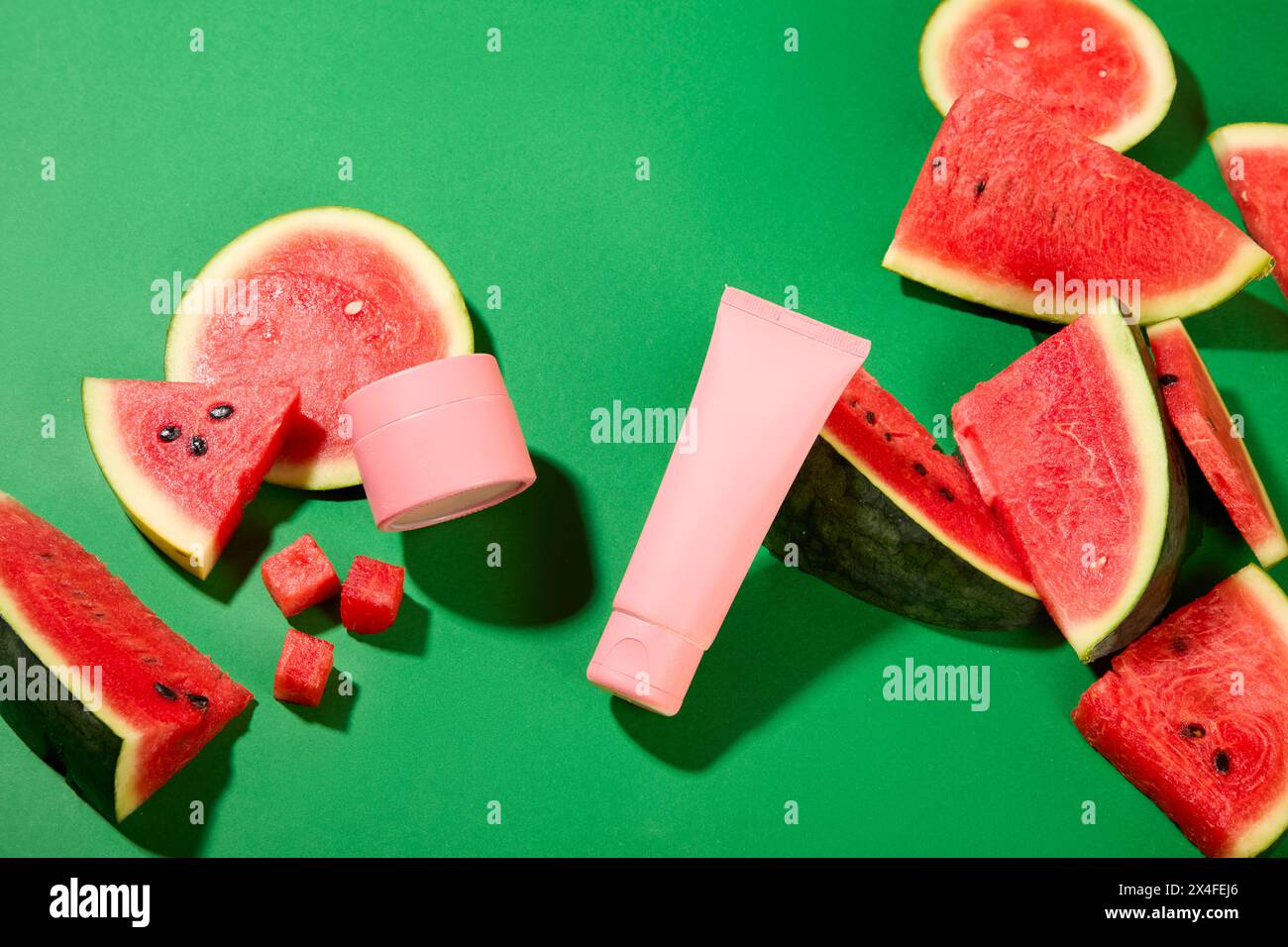 Scena per la pubblicità cosmetica con fette di anguria e set di mockup cosmetico visualizzati su sfondo verde. Ricco di antiossidanti, l'anguria è Foto Stock