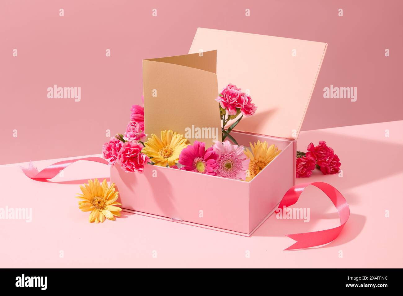 Una confezione regalo rosa riempita con la splendida gerbera, il garofano e la carta decorata su un dolce sfondo rosa. Copia spazio per il da donna internazionale Foto Stock