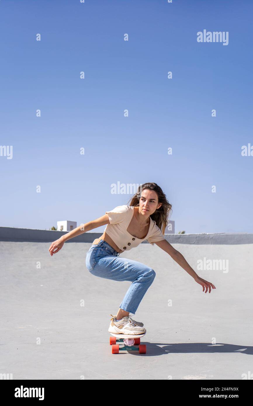 Una giovane donna sta manovrando attivamente una tavola da surf in un'area di pattinaggio all'aperto. È concentrata e si bilancia sapientemente mentre indossa CA Foto Stock