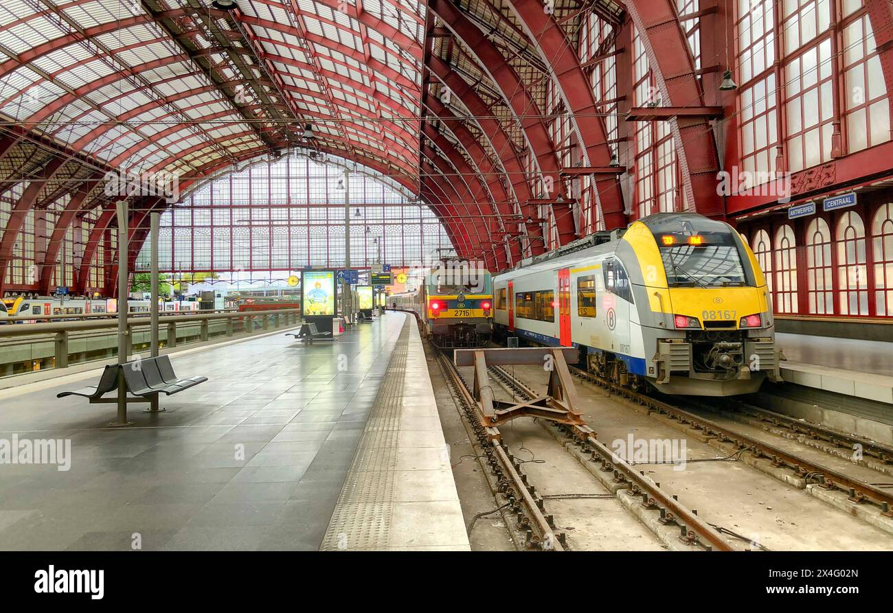 Anversa, Belgio, 13 giugno 2019, questa immagine cattura la vibrante e storica stazione ferroviaria centrale di Anversa, rinomata per il suo impressionante tetto ad arco rosso e il grande stile architettonico. Due treni moderni sono pronti sui binari, sottolineando il mix di fascino storico con soluzioni di transito contemporanee. La piattaforma è pulita, con pochi passeggeri visibili, il che suggerisce un momento tranquillo in una stazione altrimenti trafficata. Stazione ferroviaria centrale di Anversa con l'iconico tetto ad arco rosso e treni moderni. Foto di alta qualità Foto Stock