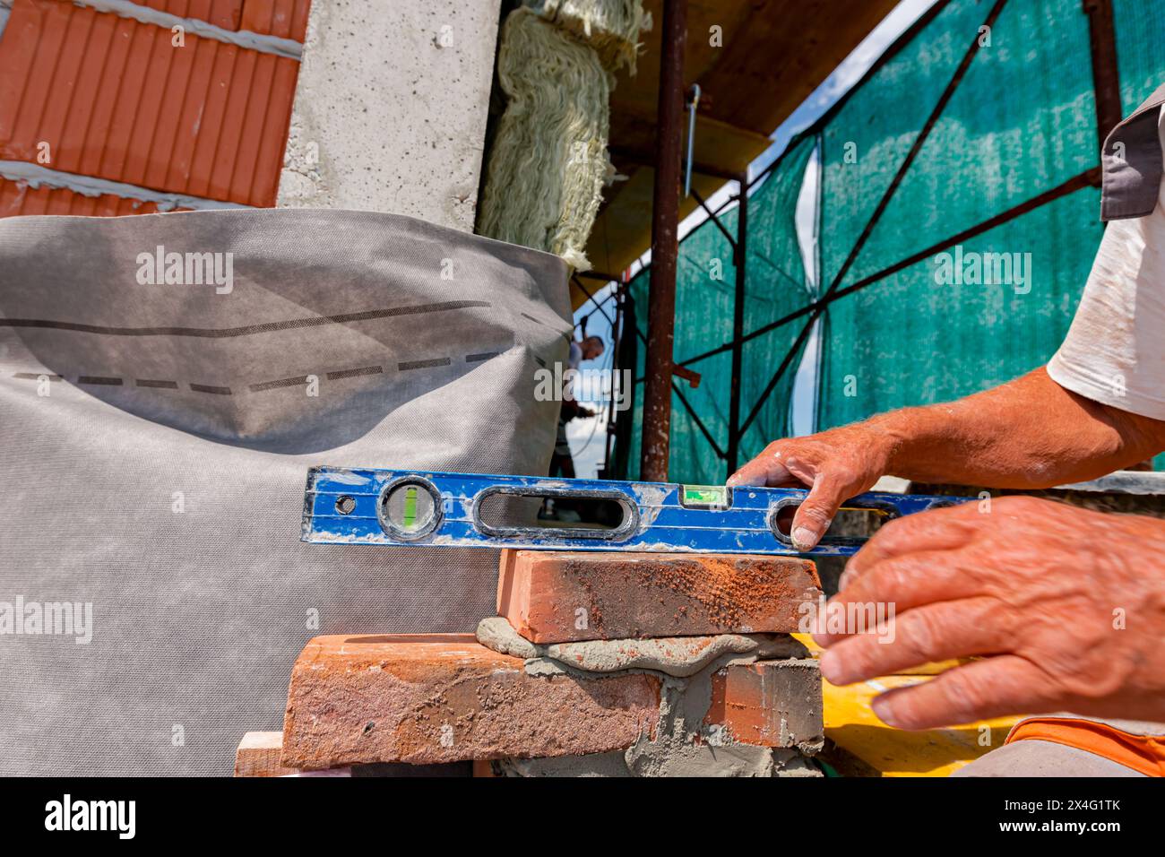 Il costruttore utilizza una livella a bolla d'aria per controllare la nuova parete in mattoni, tra fibre come tessuto isolante, strato su materiale isolante termico, lana di roccia di Foto Stock