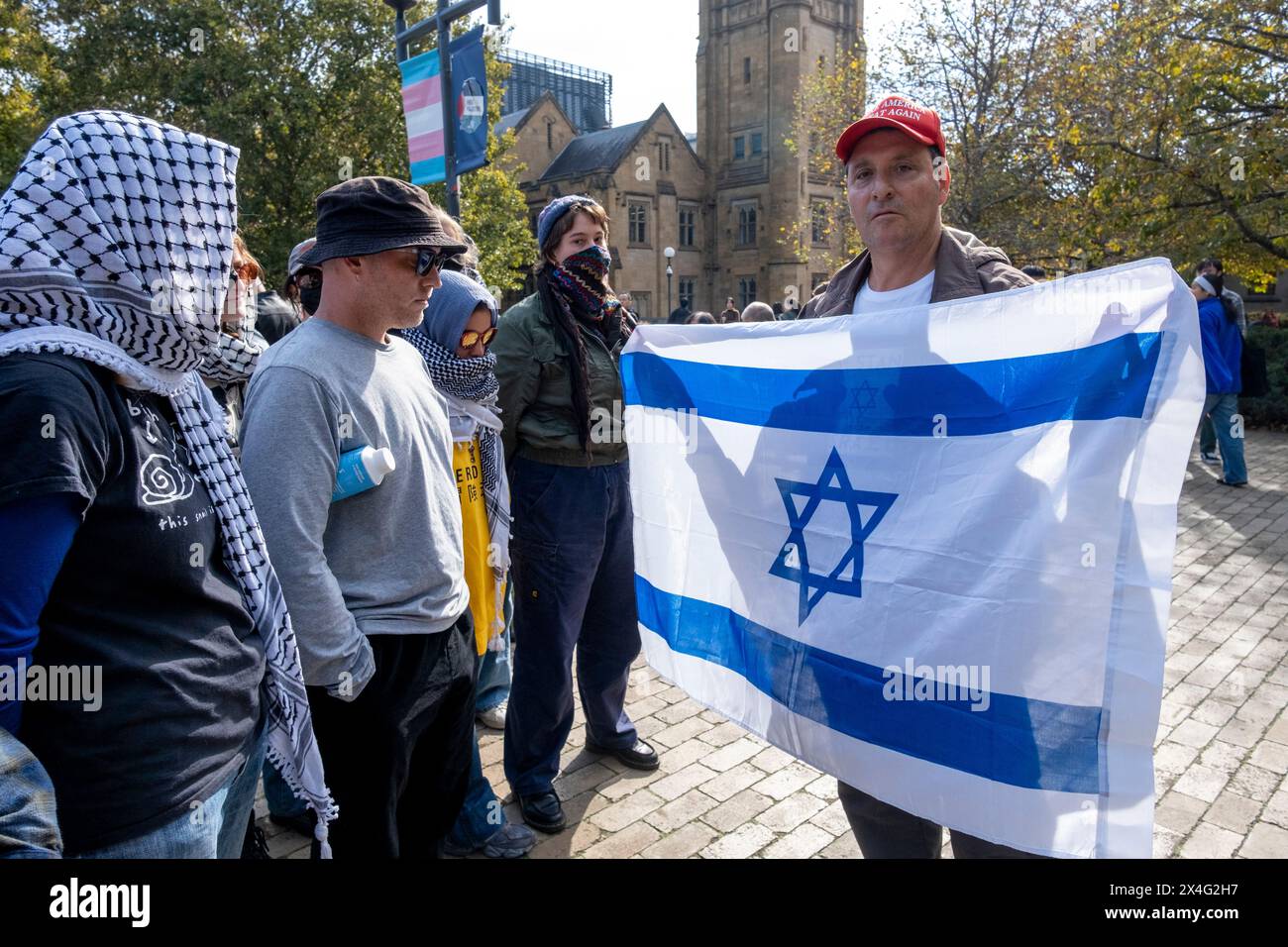 Un contro-manifestante inonda una bandiera israeliana contro i manifestanti durante una manifestazione filo-palestinese nel campus dell'Università di Melbourne. Il pro-israeliano sta indossando un berretto Make America Great Again. Melbourne, Victoria, Australia. Foto Stock