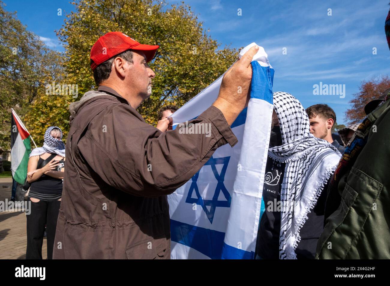 Un contro-manifestante inonda una bandiera israeliana contro i manifestanti durante una manifestazione filo-palestinese nel campus dell'Università di Melbourne. Il pro-israeliano sta indossando un berretto Make America Great Again. Melbourne, Victoria, Australia. Foto Stock