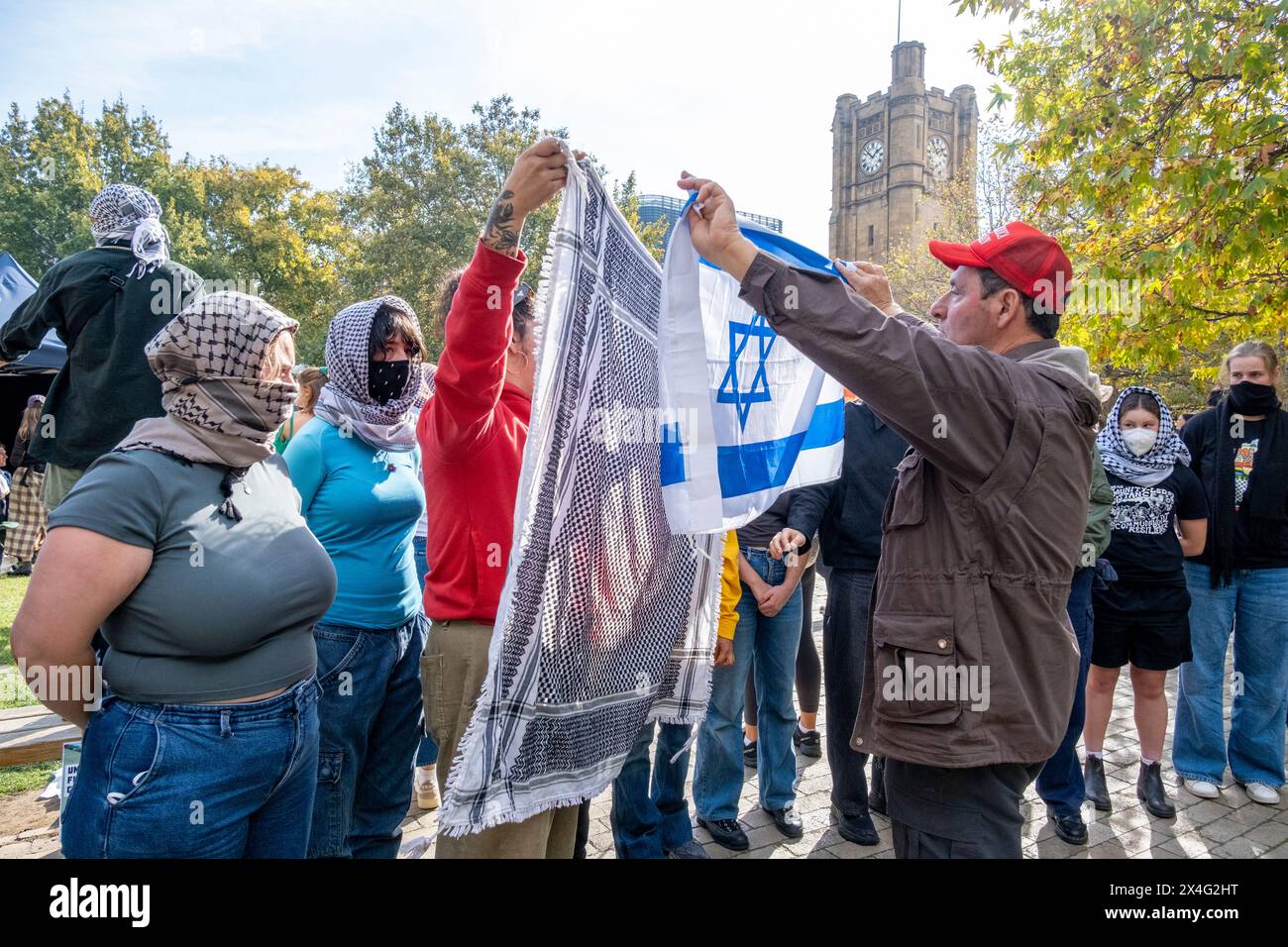 Un contro-manifestante inonda una bandiera israeliana contro i manifestanti durante una manifestazione filo-palestinese nel campus dell'Università di Melbourne. Il pro-israeliano sta indossando un berretto Make America Great Again. Melbourne, Victoria, Australia. Foto Stock