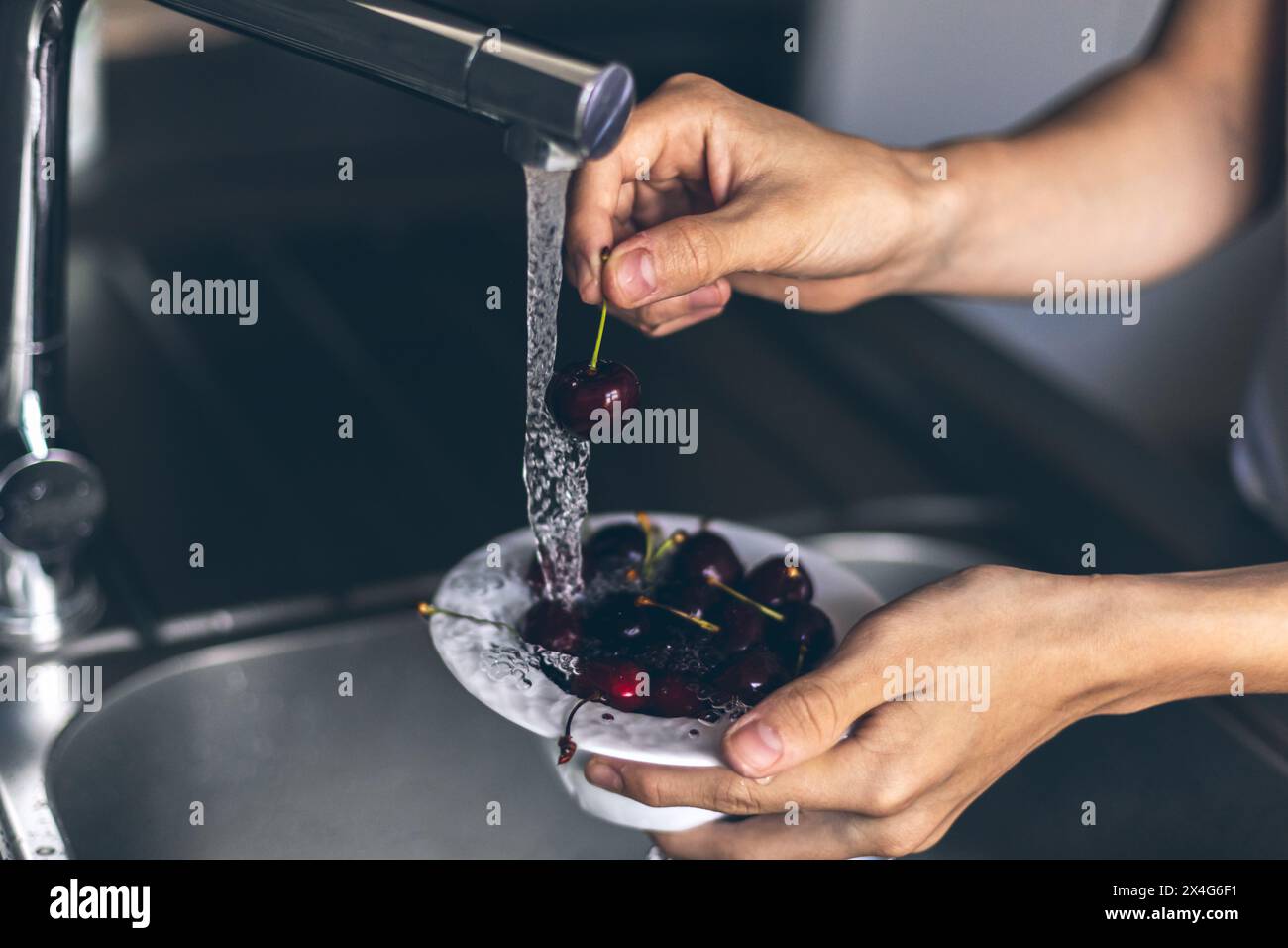 Sezione centrale delle mani umane che lava la ciliegia dolce fresca Foto Stock