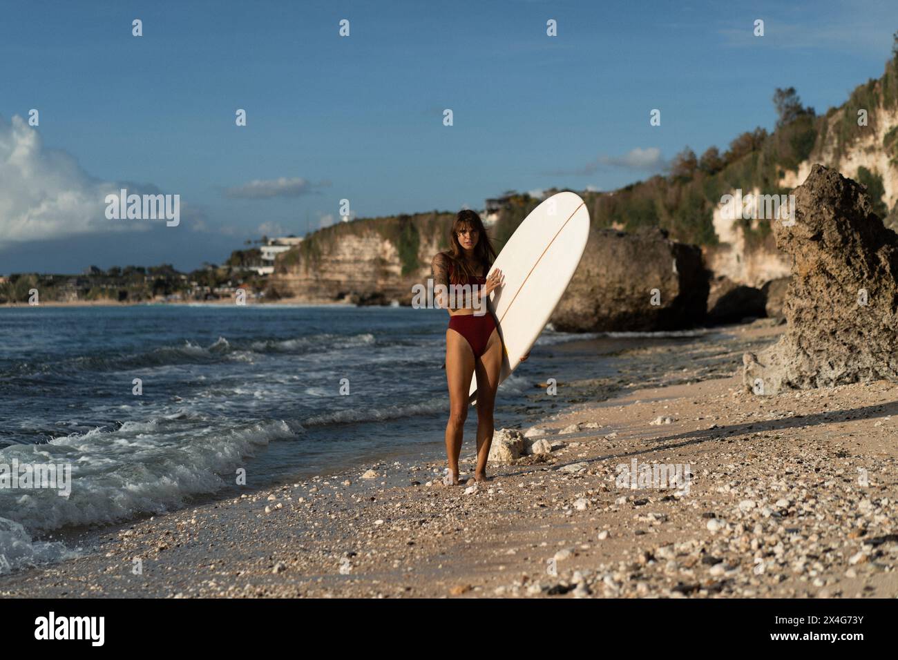 Giovane donna con tavola da surf su una spiaggia. Foto Stock