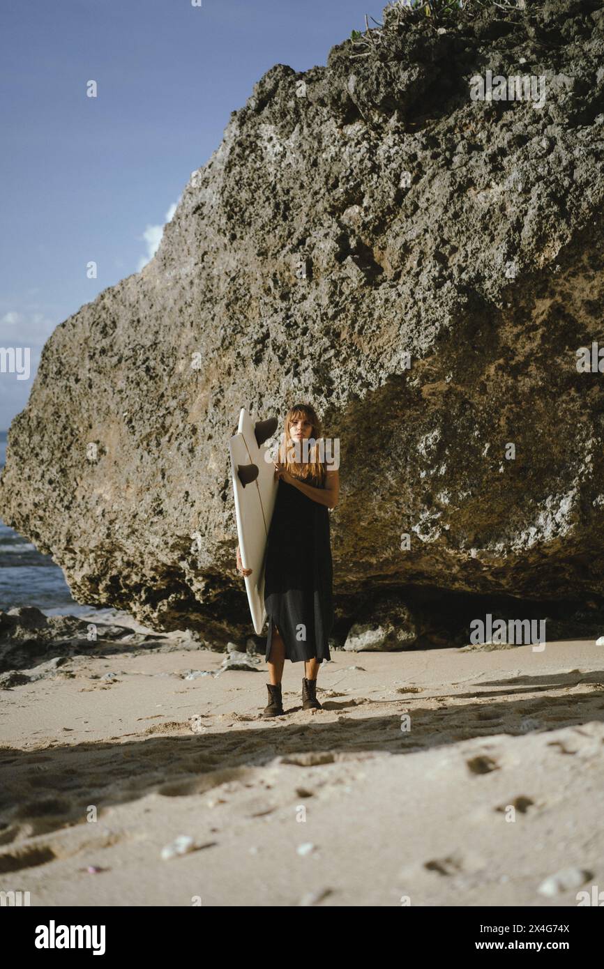Donna con tavola da surf in piedi sulla spiaggia Foto Stock