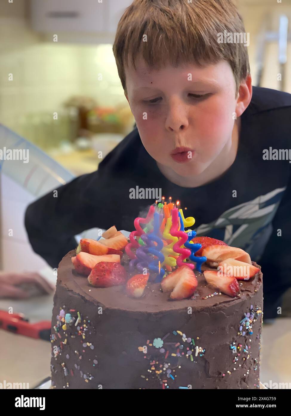 Il ragazzo fa saltare le candele su una torta di compleanno al cioccolato Foto Stock