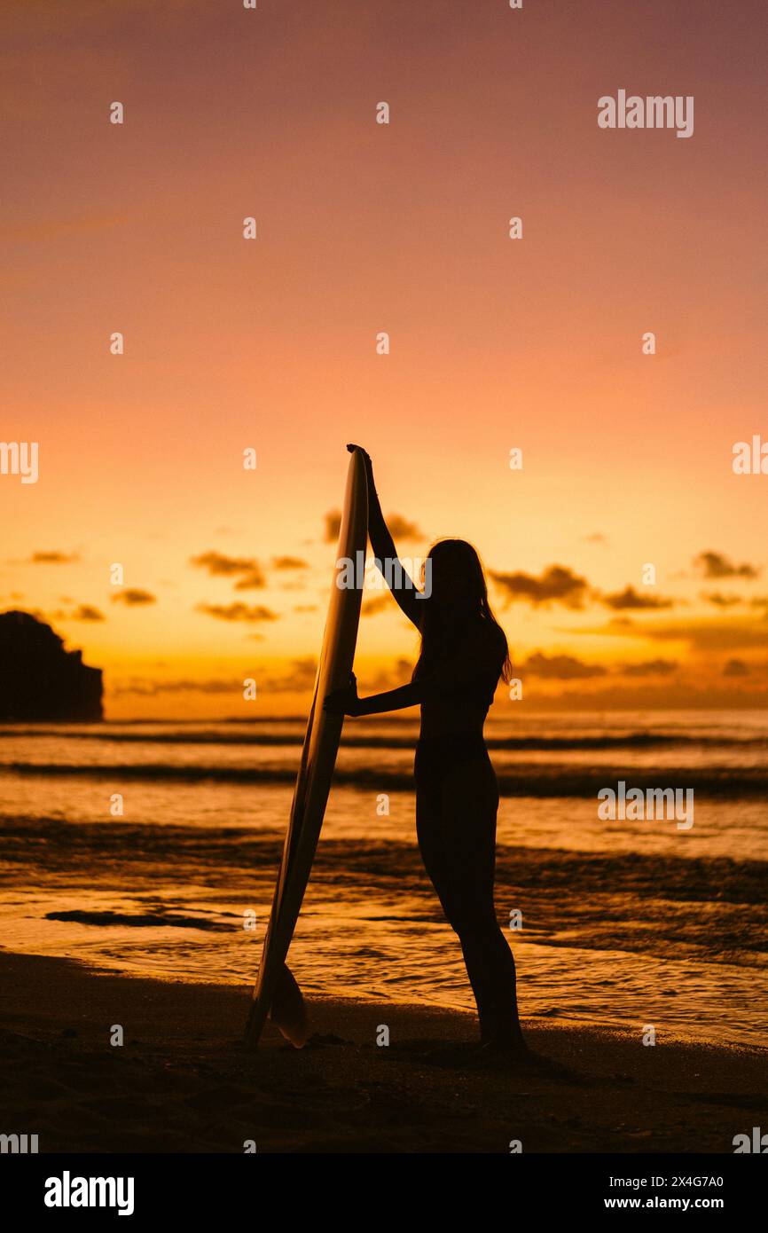 Lunghezza intera della silhouette giovane donna con tavola da surf in piedi sulla spiaggia Foto Stock