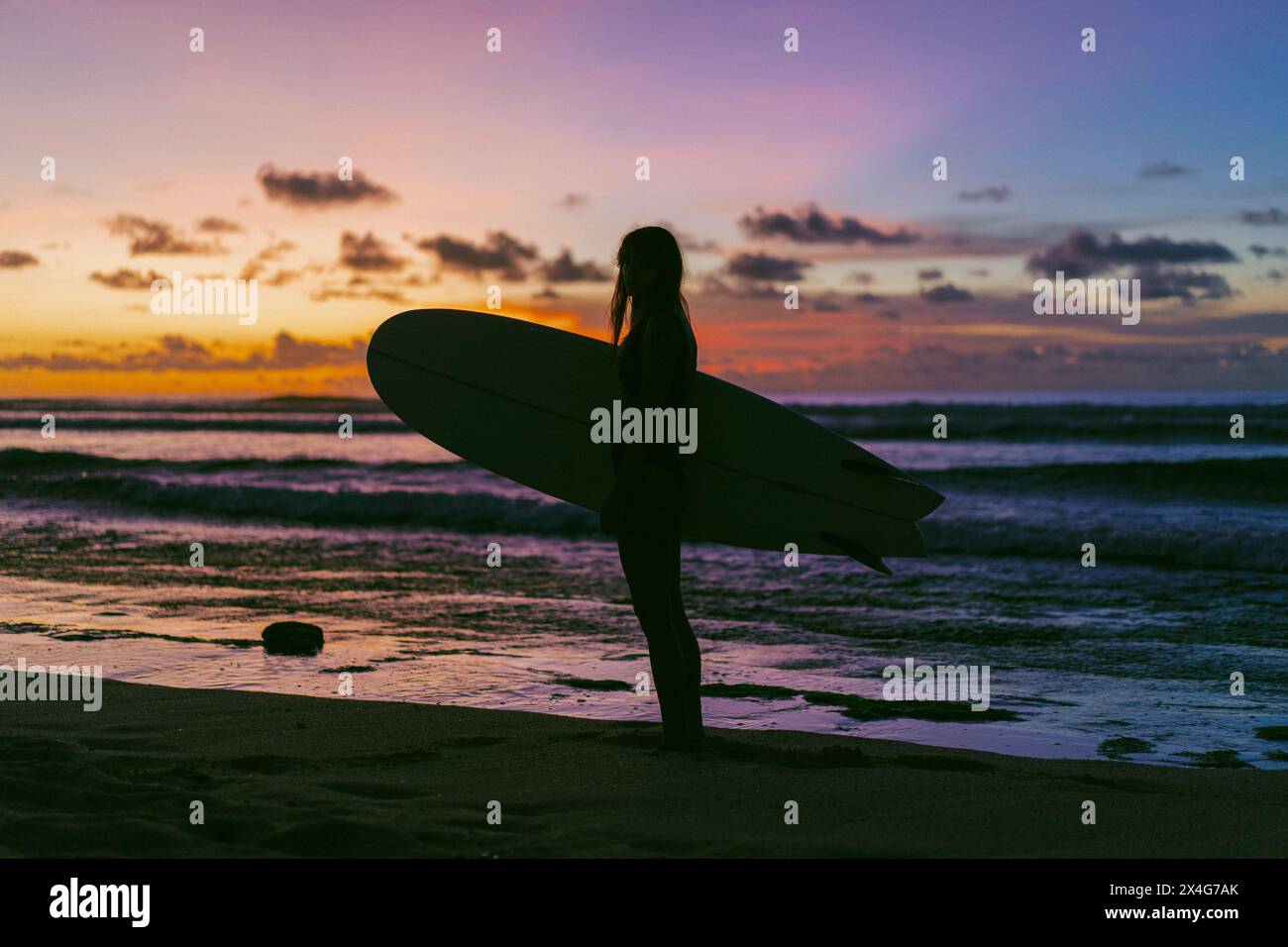 Donna con la tavola da surf relax in spiaggia durante il tramonto Foto Stock
