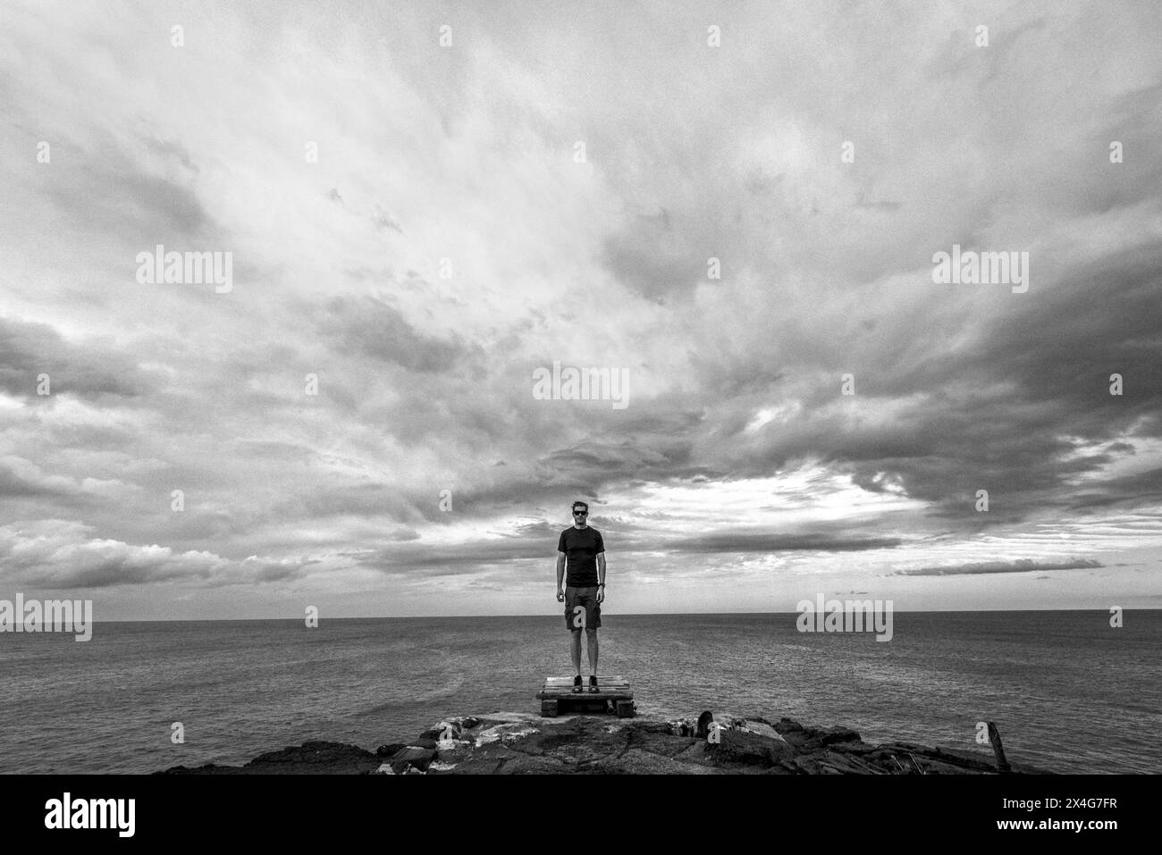 L'uomo in pantaloncini è sul bordo della scogliera di fronte all'Oceano Pacifico Foto Stock