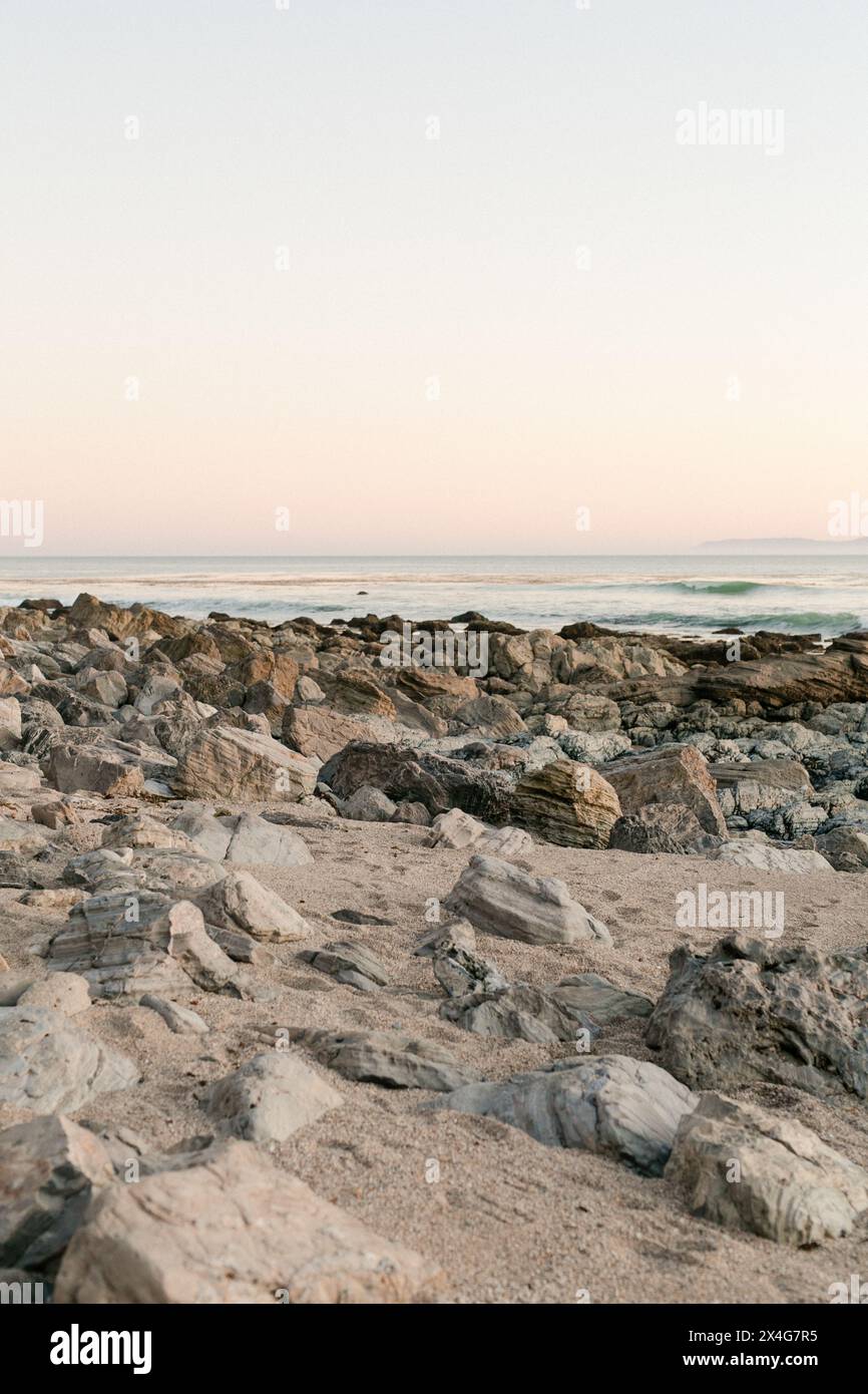 Il crepuscolo pastello si adagia su una tranquilla costa rocciosa Foto Stock