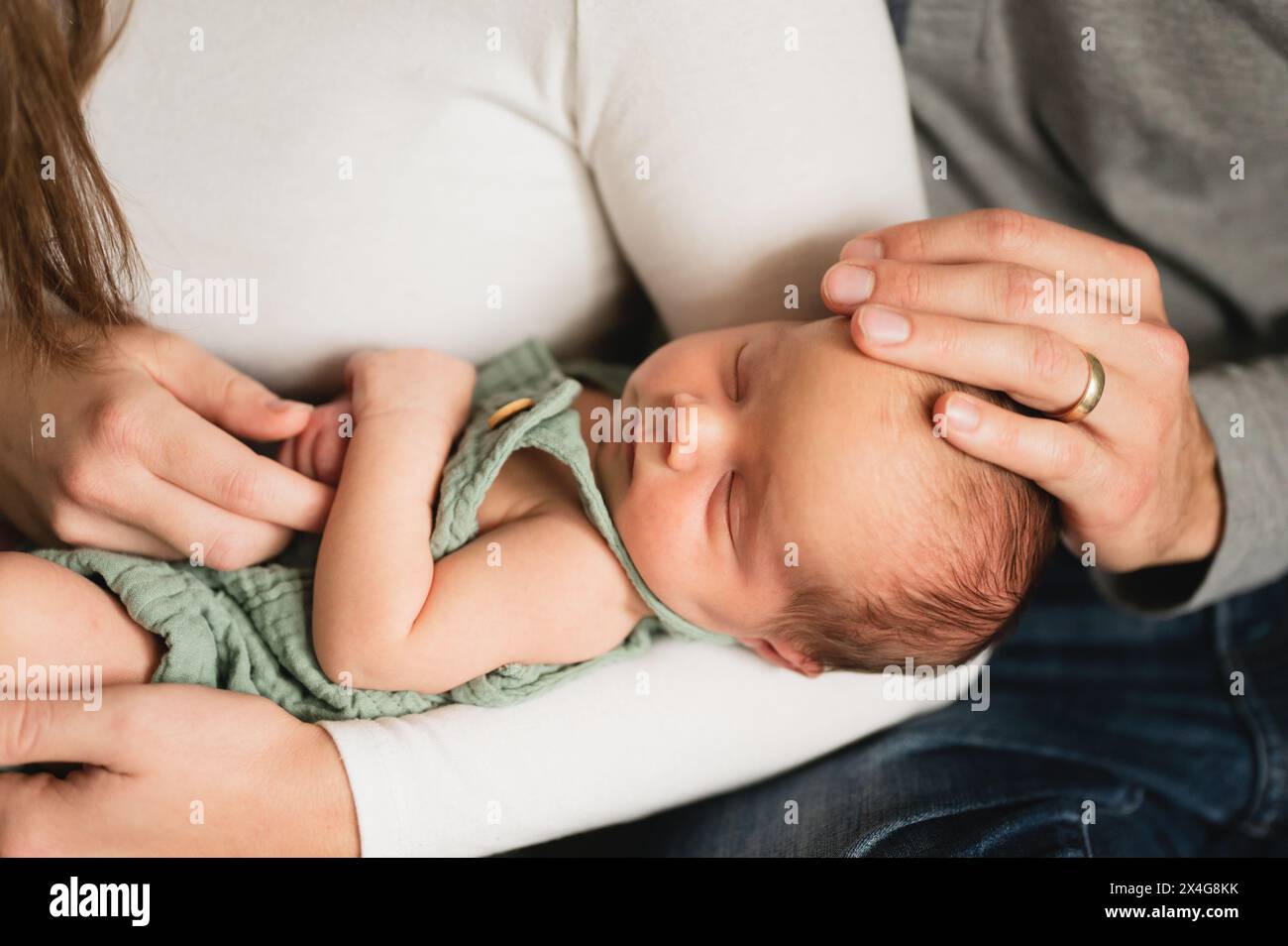 Primo piano delle mani di padre e madre sposati che tengono il bambino in braccio Foto Stock