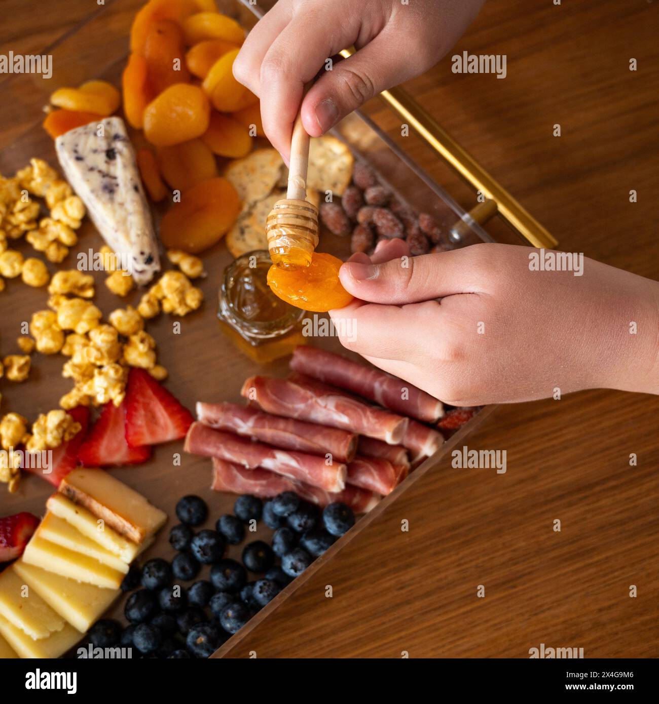 Mani che immergono il miele sulla frutta; vari e colorati salumi spalmabili. Foto Stock
