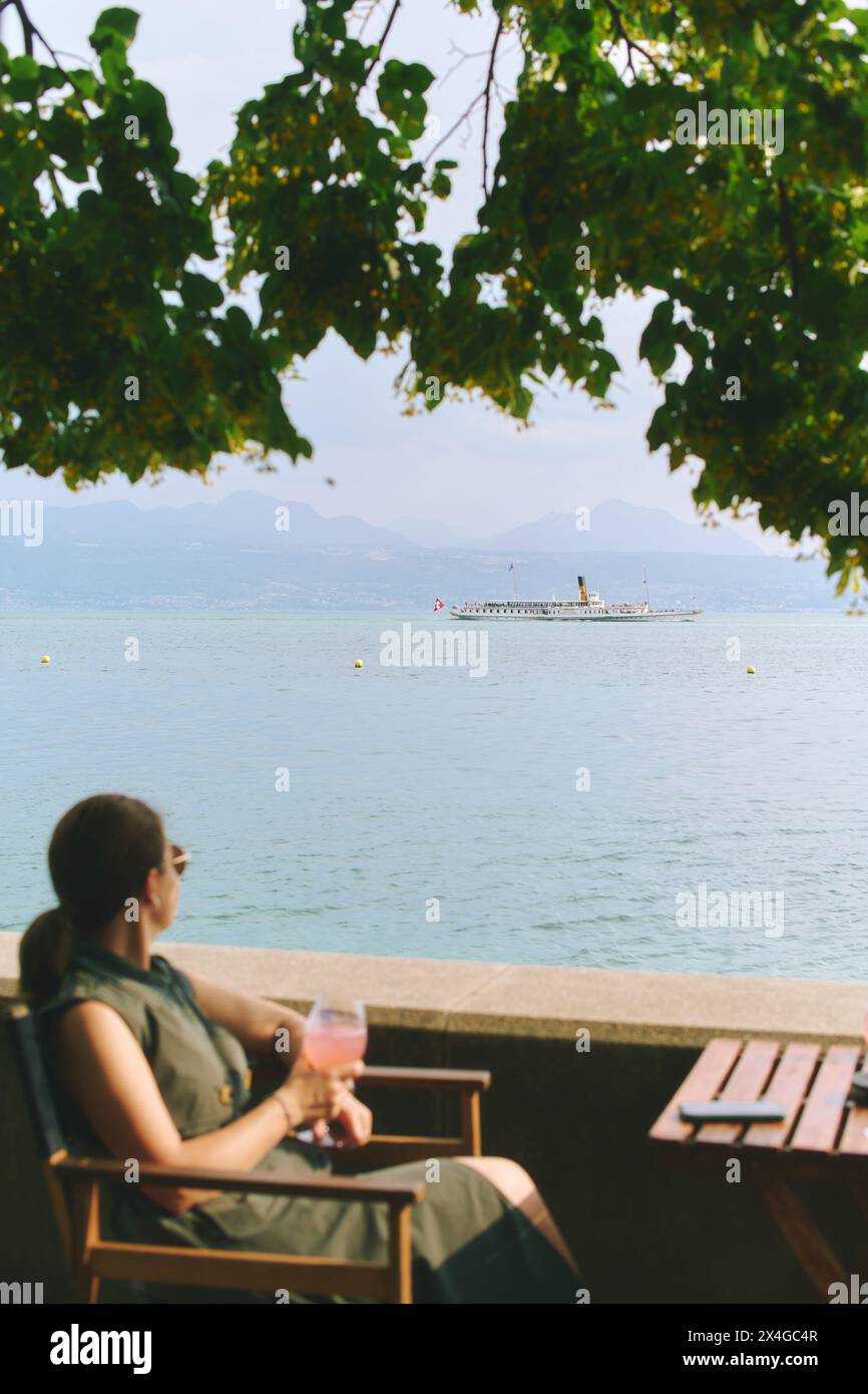Vista con la barca galleggiante sul lago di Ginevra, Svizzera, vista dal ristorante estivo o dal bar con donna che si rilassa sulla terrazza con un bicchiere di vite, vacanza Foto Stock
