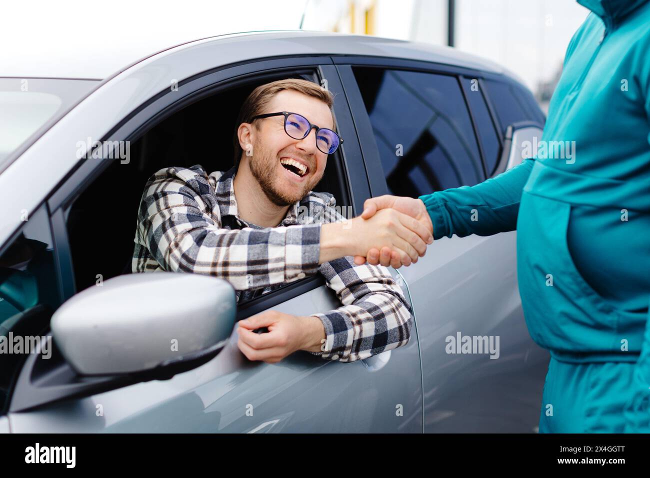 Uomo che compra auto e stringe la mano al venditore contro auto offuscate, primo piano. Concetto di scelta e acquisto di una nuova vettura presso lo showroom. Foto Stock